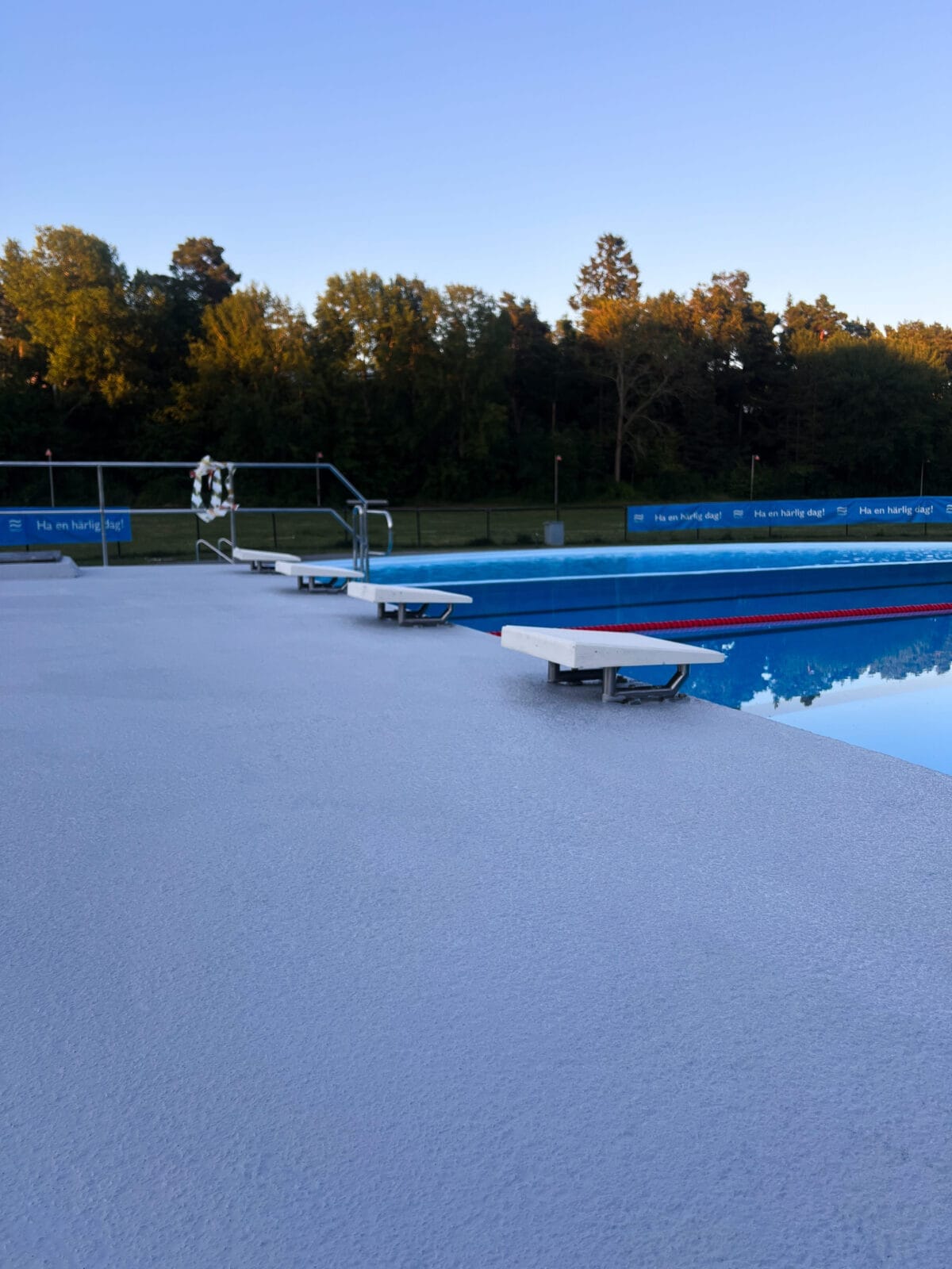 bredare perspektiv av en blå halkskyddsmålad poolkant med startpallar och en simbassäng.