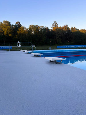bredare perspektiv av en blå halkskyddsmålad poolkant med startpallar och en simbassäng.