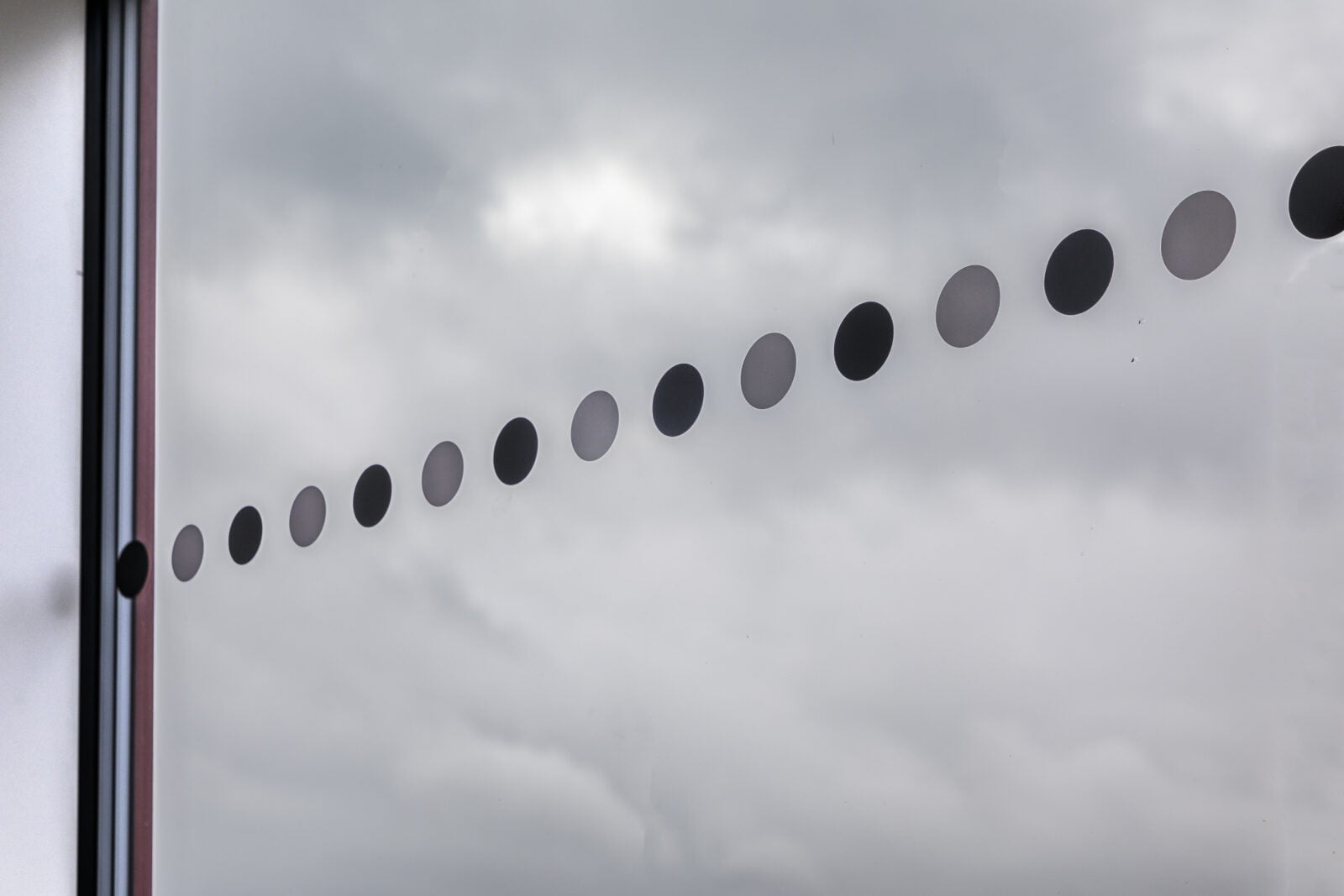 Kontrastmarkeringar i form av alternerande svarta och gråa cirklar i en horisontell linje på glasyta mot molnig himmel.