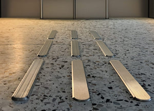 Taktila ledstråk i rostfritt stål med räfflad struktur installerade i ett terrazzogolv. Ledstavarna bildar tre parallella linjer.