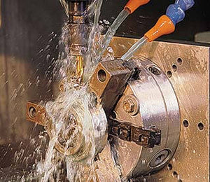 Närbild av maskinbearbetning med skärvätska som bildar vitt skum och stänk över metallytan under skärningsprocessen.