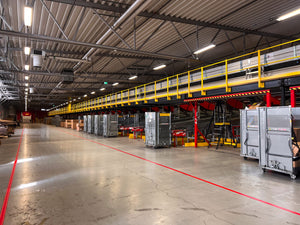 Industrilokal med gul säkerhetsräcke, röd Safestep Linjemålning och logistikcontainrar i lagerbyggnad.