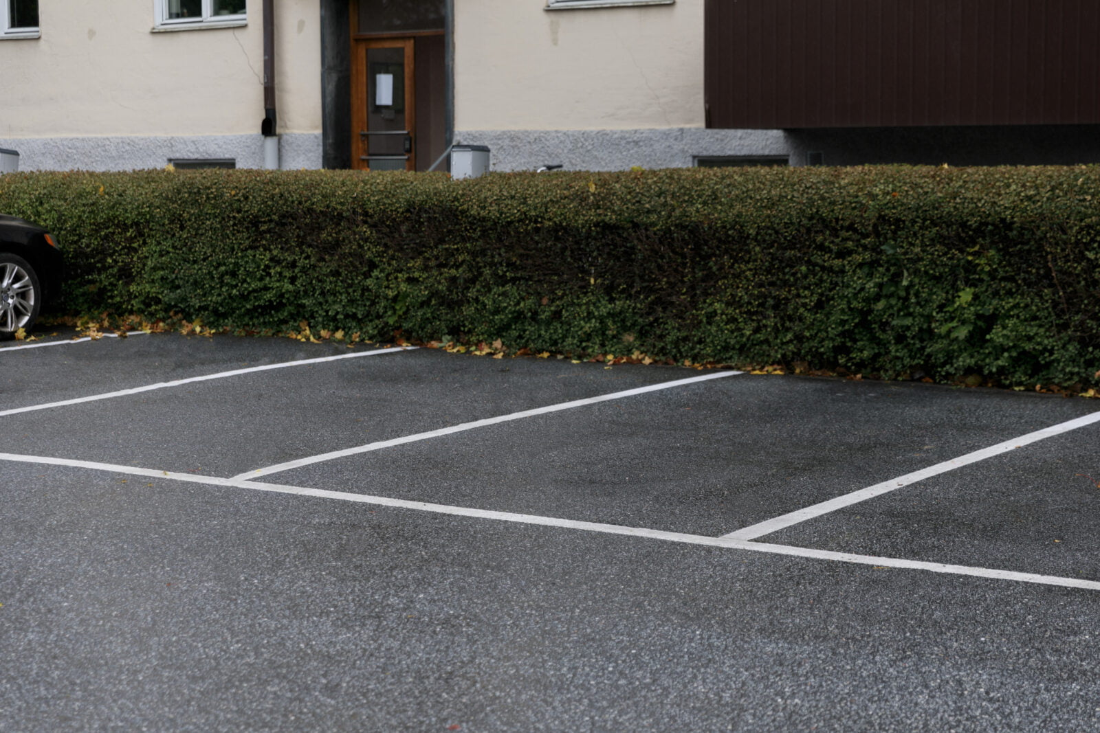 Parkeringsplatser med tydlig vit Safestep Linjemålning intill häck och bostadsfastighet.
