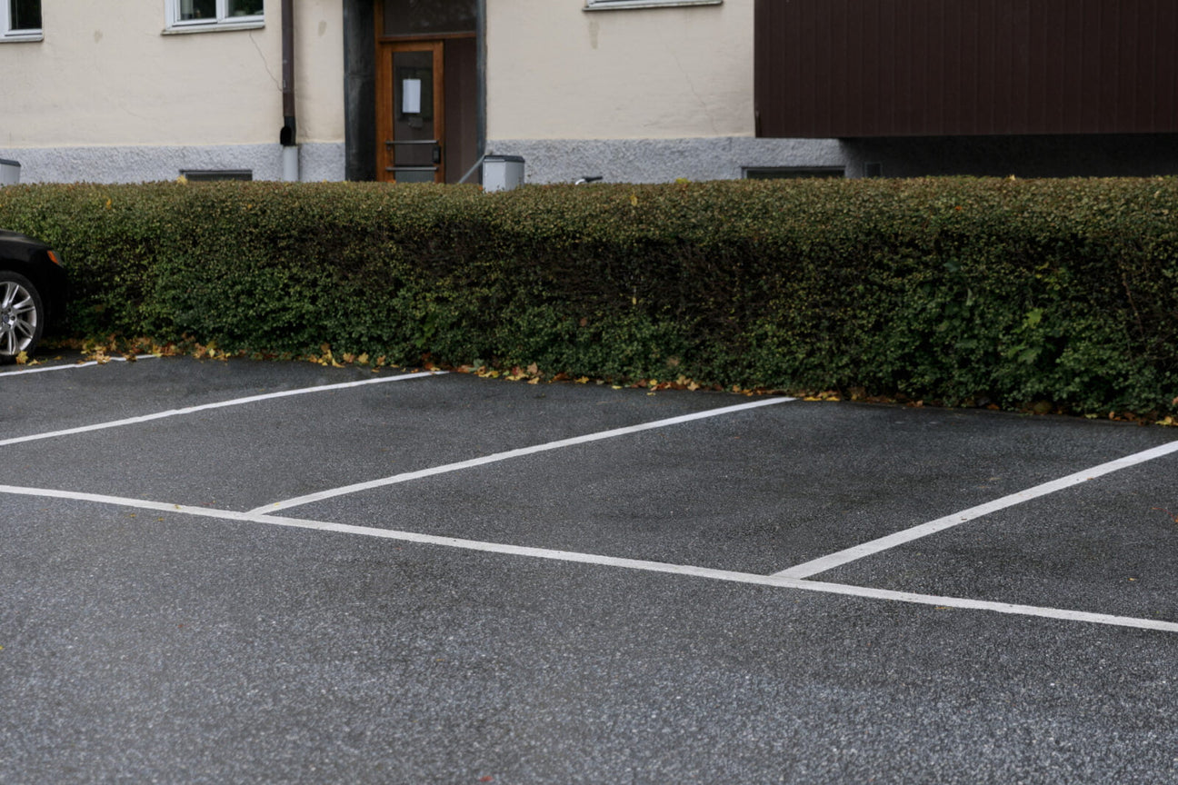Parkeringsplatser med tydlig vit Safestep Linjemålning intill häck och bostadsfastighet.
