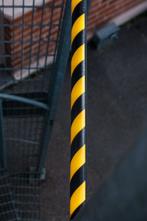Närbild på svart/gul skyddslist med diagonala varningsränder monterad på metallstolpe.