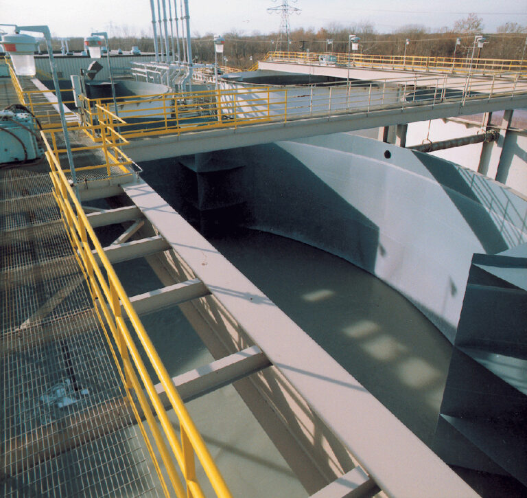 Industriell anläggning med gångbryggor och gula räcken. Betongkanal eller tank med Chesterton ARC S1HB korrosionsskyddande beläggning.