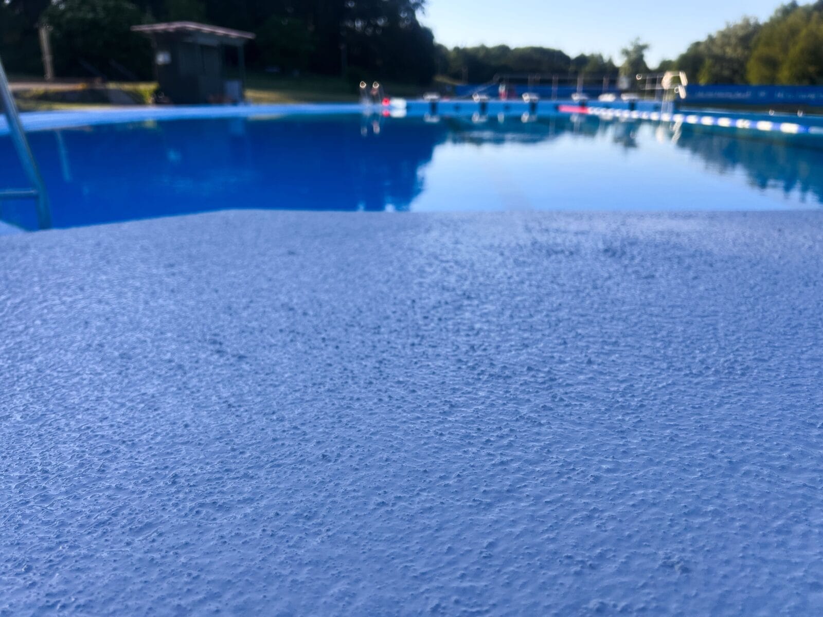 närbild av en blå halkskyddsmålad yta runt en utomhuspool.