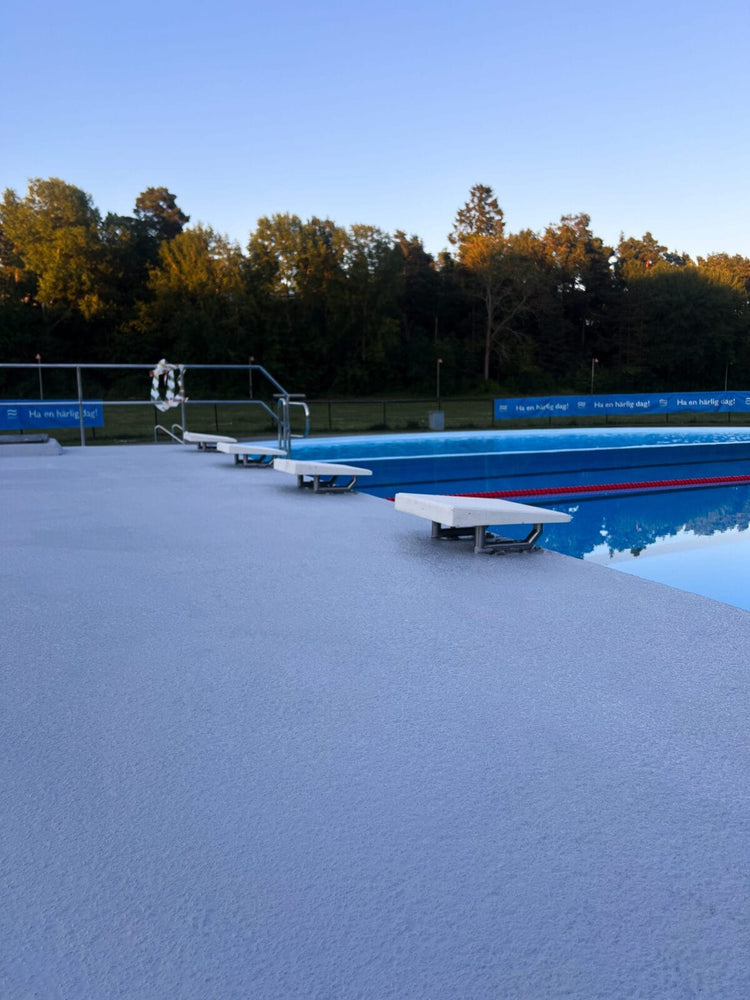 bredare perspektiv av en blå halkskyddsmålad poolkant med startpallar och en simbassäng.