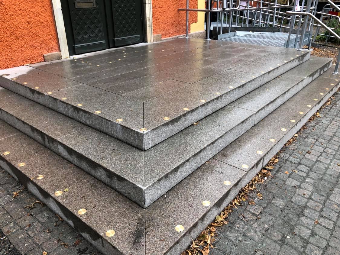 Trappa med ljusa kontrastmarkeringar längs framkanten av varje steg som leder upp till en orange byggnad 