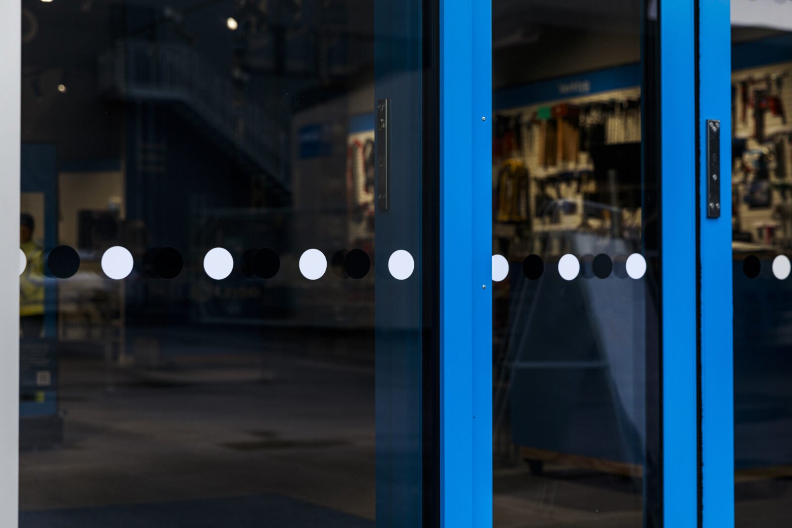 Kontrastmarkeringar bestående av omväxlande svarta och vita cirklar på glasdörr med blå ram till en butikslokal.