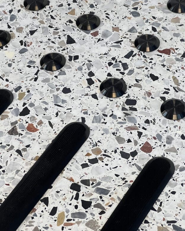 Taktila stoppmarkeringar med svart PVD-beläggning på rostfritt stål monterade i ett ljust terrazzogolv.
