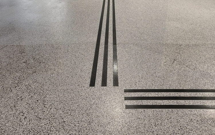 Mörka aluminiumprofiler bildar taktila ledstråk med korsande linjer på ljust terrazzogolv för navigering i offentlig miljö.